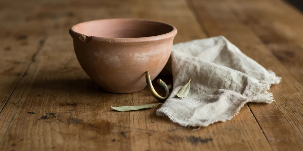 A chipped unglazed clay bowl and a softened linen cloth on an oak surface marked by years of use