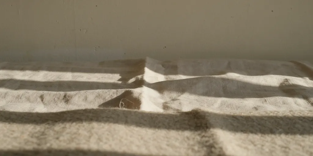 Close view of deeply creased unbleached linen, the visible pile of an undyed wool blanket and a matte lime plaster wall, all in the same warm off-white family