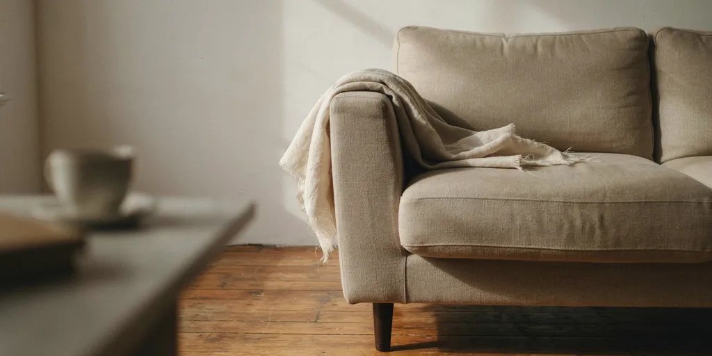 A reading chair with exactly one undyed wool throw pushed to the side of the seat and nothing else on it