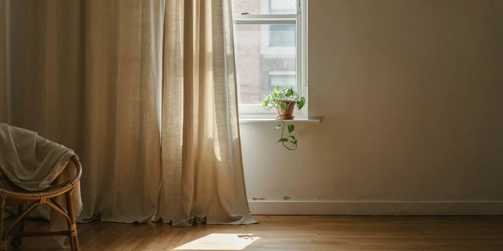 Oat linen curtains hung from a rod fixed under the ceiling and falling to the floor, more than twice the height of the short window behind them