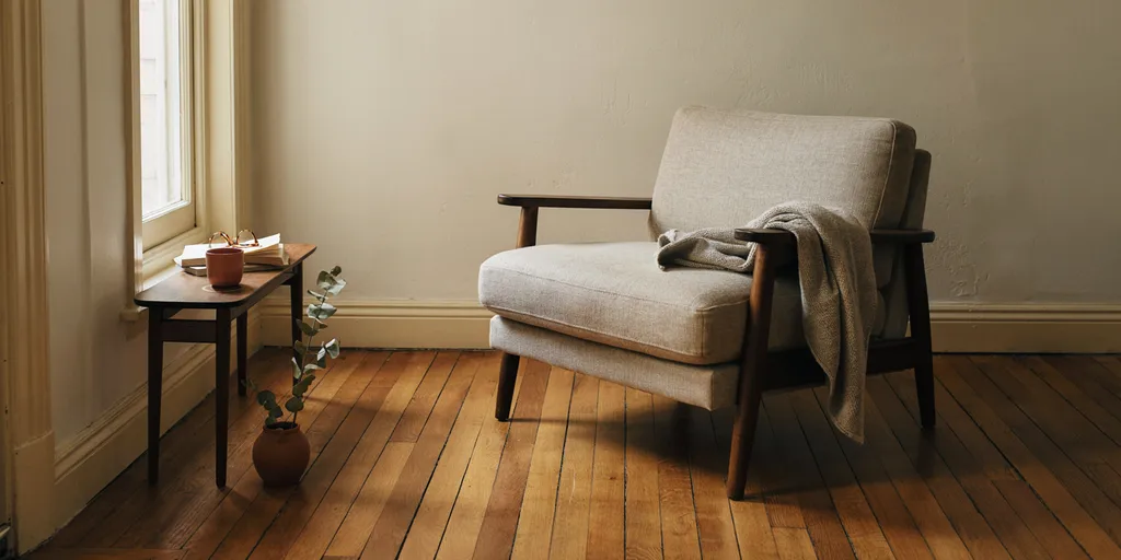 A single large deep armchair in oat linen with a walnut frame, noticeably bigger than everything around it