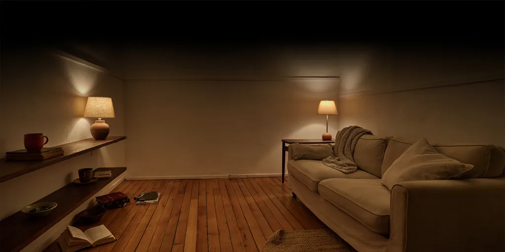 A small living room after dark lit only by three warm lamps below eye level, their pools of light reaching into the corners while the ceiling stays dark