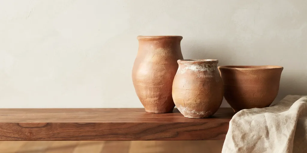 Three unglazed terracotta vessels of different heights on a walnut shelf in low warm side light