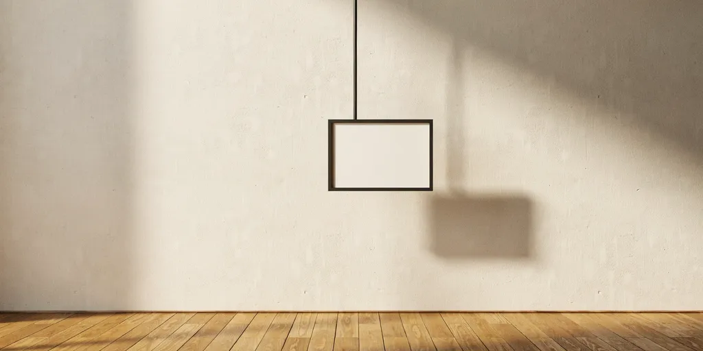 A small picture in a slim black frame hanging from a thin black line against warm off-white plaster
