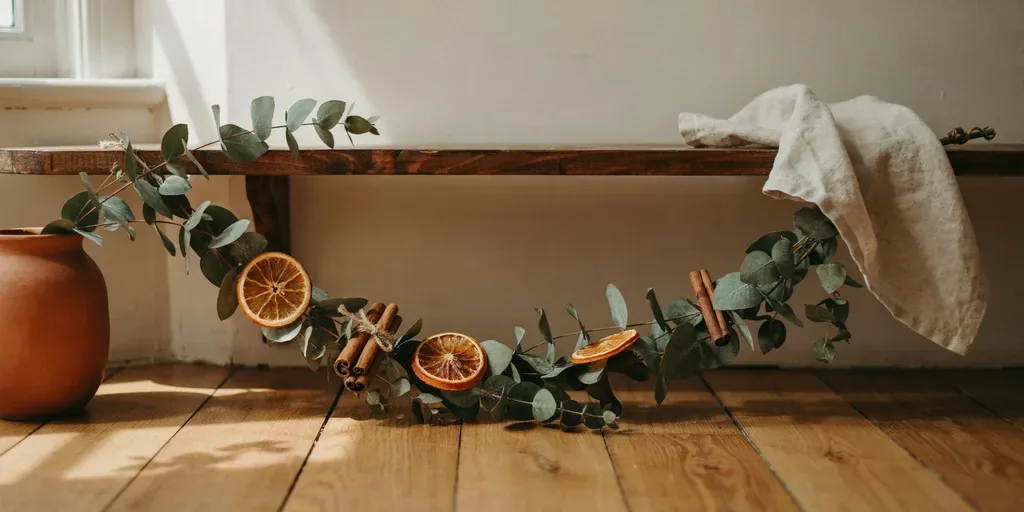 A eucalyptus garland on a mantel with dried orange slices tucked into it and a few cinnamon sticks